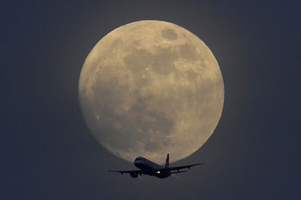 Самолет на фоне полной луны в небе над Лондоном, Великобритания