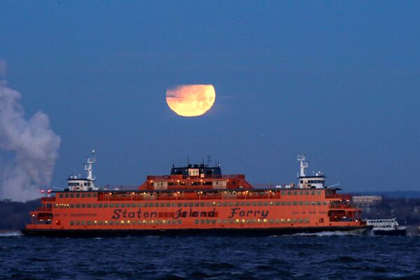 Полная луна садится позади парома на остров Статен-Айленд, США
