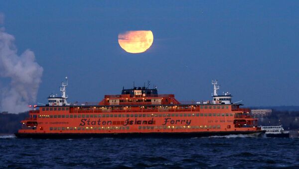 Полная луна садится позади парома на остров Статен-Айленд, США