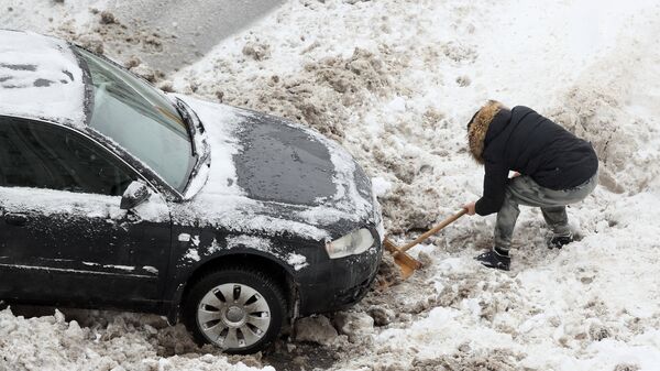 Водитель откапывает из снега свою машину после снегопада