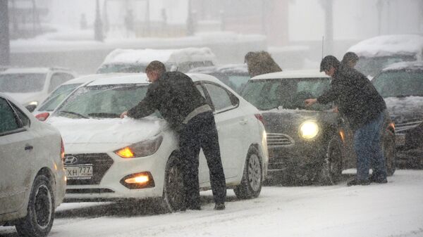 Владельцы отчищают свои машины от налипшего снега во время снегопада. Архивное фото