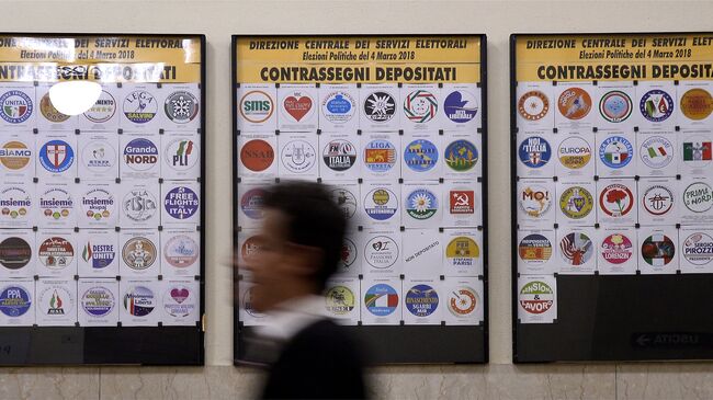 Мужчина проходит мимо доски с логотипами партий, зарегистрированных в преддверии выборов в Италии. 20 января 2018 года