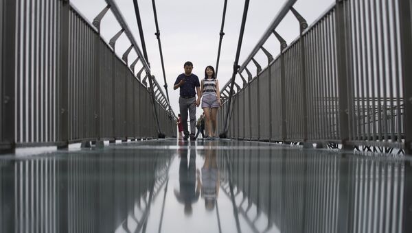 Пара идет по стеклянной дорожке, которая считается самой длиннойм в мире, в парке Ордовик в Ваншэн, Китай. 1 июня 2017