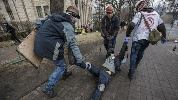 Сторонники оппозиции несут раненного во время столкновений с сотрудниками правопорядка на улице Институской в Киеве