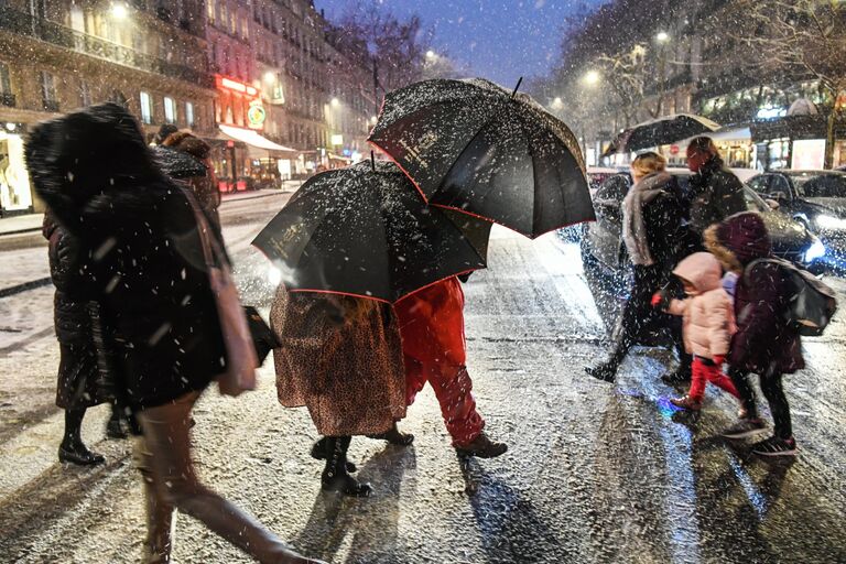 Прохожие на пешеходном переходе во время снегопада в Париже