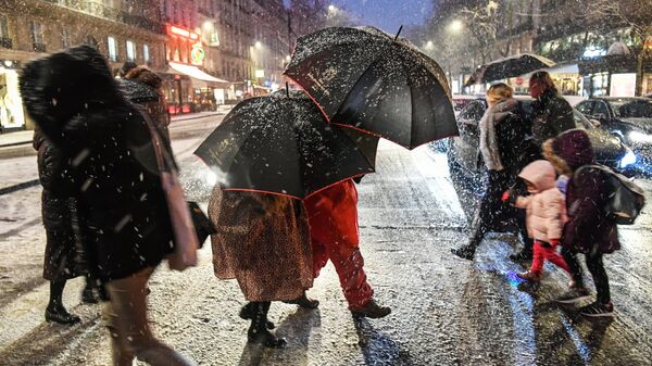 Прохожие на пешеходном переходе во время снегопада в Париже