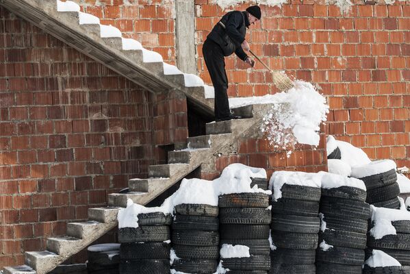 Мужчина убирает снег с лестницы своего дома после снегопада в Косово