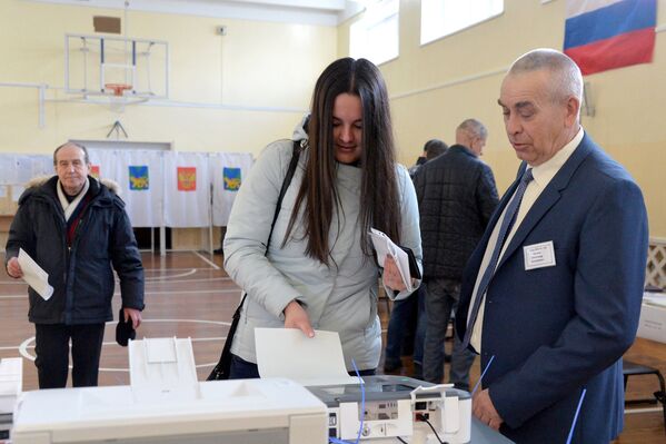 Девушка опускает бюллетень в урну на выборах президента РФ на избирательном участке во Владивостоке.