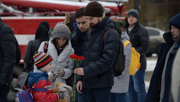 Люди несут цветы, свечи и мягкие игрушки к зданию торгового центра «Зимняя вишня» в Кемерово, где произошел пожар