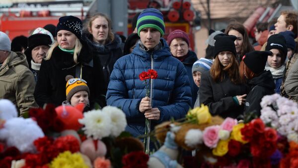 Жители несут цветы и мягкие игрушки к зданию торгового центра «Зимняя вишня» в Кемерово, где произошел пожар