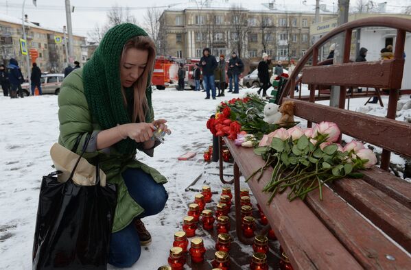 Женщина зажигает свечу возле здания торгового центра «Зимняя вишня» в Кемерово, где произошел пожар