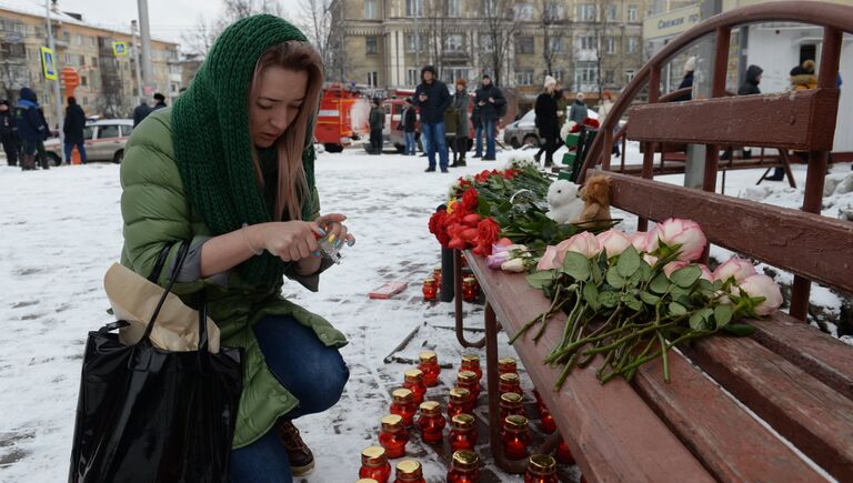 Женщина зажигает свечу возле здания торгового центра «Зимняя вишня» в Кемерово, где произошел пожар