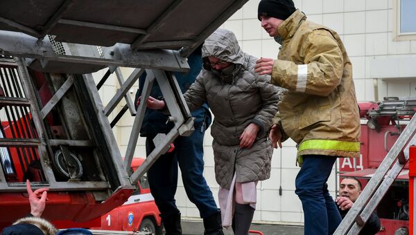Сотрудники пожарной охраны МЧС помогают посетителям выбраться из торгового центра Зимняя вишня в Кемерово, где произошел пожар