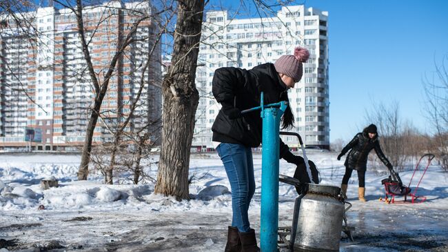 Женщина набирает воду в бидон из колонки