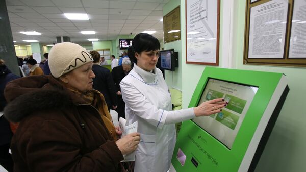 Сотрудница московской поликлиники помогает женщине записаться на прием к врачу через электронную регистратуру