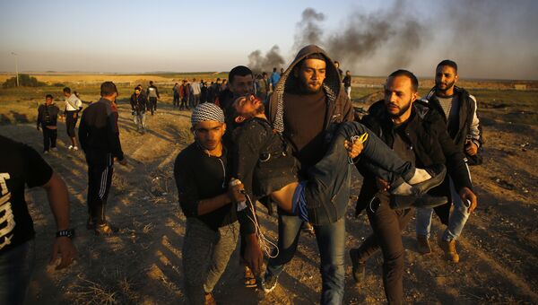 Палестинские демонстранты несут раненого во время столкновений с израильскими силами вдоль границы с Израилем к востоку от Газы. 1 апреля 2018