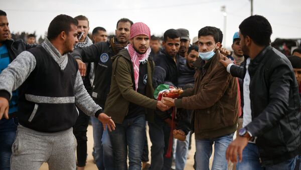 Палестинские протестующие несут пострадавшего во время столкновений с израильскими военными на границе сектора Газа и Израиля. Архивное фото