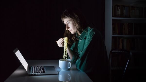 Девушка ест лапшу быстрого приготовления перед экраном ноутбука 