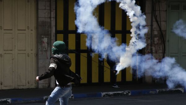 Палестинский демонстрант отбрасывает канистру со слезоточивым газом в сторону израильских сил во время столкновений в Хевроне. 31 марта 2018