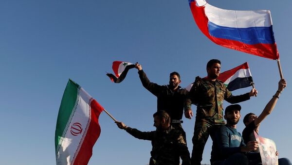 Сирийцы размахивают иранскими, российскими и сирийскими флагами, протестуя против воздушных ударов коалиции под командованием США в Дамаске, 14 апреля 2018