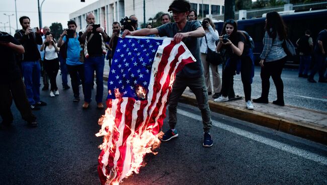 Сожжение флага США перед зданием посольства Сша в  Афинах в Греции. 14 апреля 2018