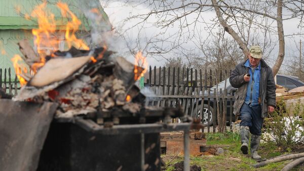 Мужчина сжигает мусор в баке на дачном участке