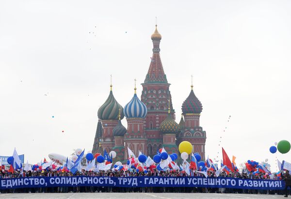 Участники первомайской демонстрации несут плакат Единство, солидарность, труд - гарантия успешного развития на Красной площади в Москве