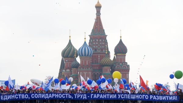 Участники первомайской демонстрации несут плакат Единство, солидарность, труд - гарантия успешного развития на Красной площади в Москве