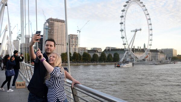 Туристы фотографируются на фоне Колеса обозрения Лондонский глаз на берегу Темзы в Лондоне