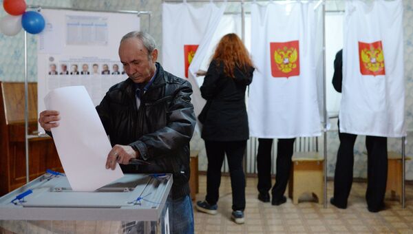 Мужчина опускает бюллетень во время голосования на выборах президента России на избирательном участке в Крыму