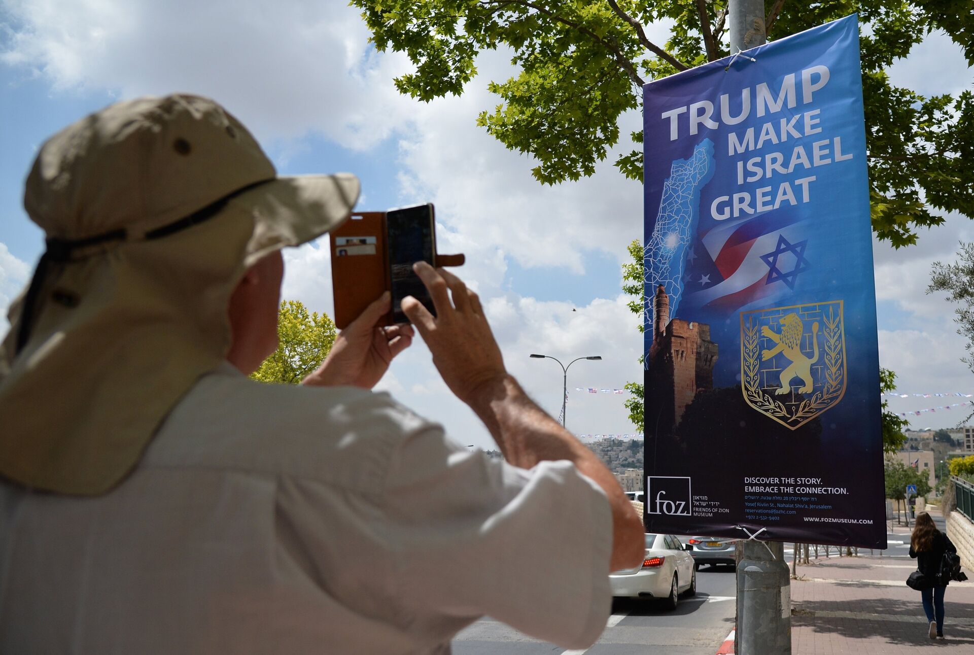 Мужчина фотографирует баннер, посвященный церемонии переноса посольства США из Тель-Авива в Иерусалим - РИА Новости, 1920, 19.05.2021