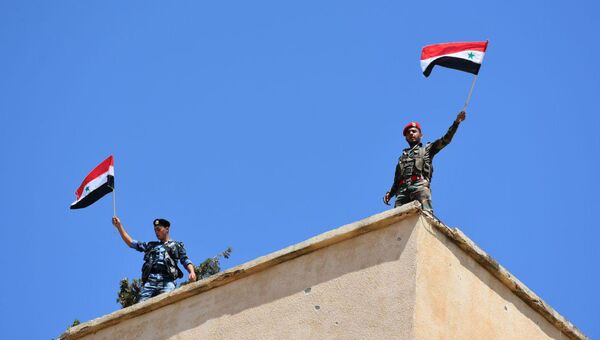 Сирийские военные с флагами в освобожденном от боевиков населенном пункте в провинции Хомс