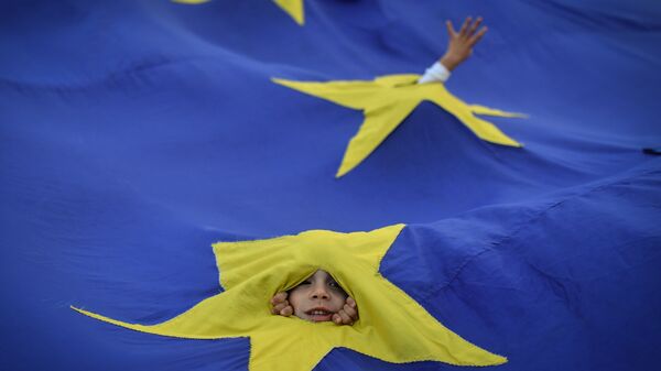 Дети выглядывают из прорезей во флаге ЕС во время акции протеста в Бухаресте, Румыния