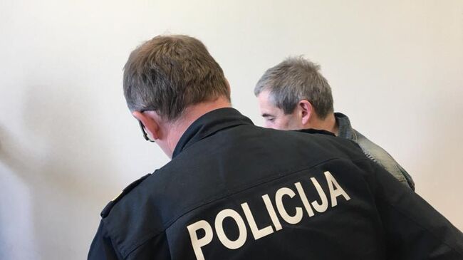 Сотрудник полиции ведет Владимира Линдермана в зал заседаний суда в Риге 