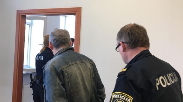 Сотрудник полиции ведет Владимира Линдермана в зал заседаний суда в Риге