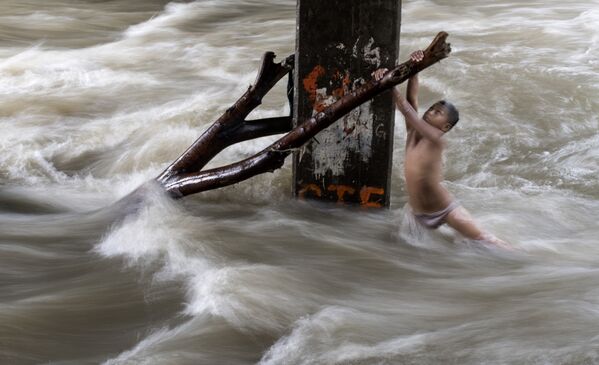 Мальчик держится за ветку во время игры в переполненной сильными дождями реке в Маниле