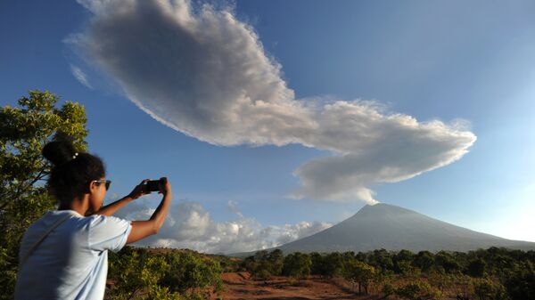 Девушка фотографирует столб дыма, выброшенный из вулкана Агунг в Индонезии 