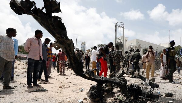 Офицеры безопасности Сомали и гражданские лица смотрят на обломки автомобиля на месте взрыва вблизи президентского дворца в Могадишо. 14 июля 2018