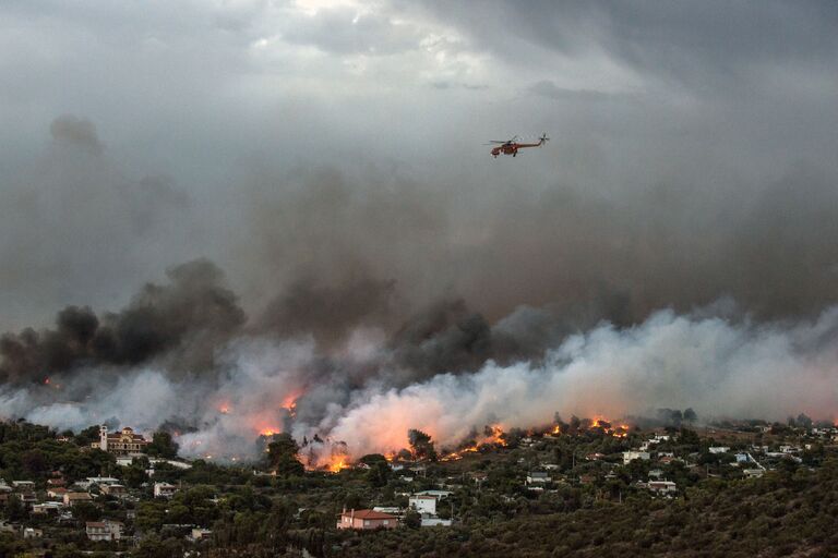Пожарный вертолет пролетает над лесным пожаром в городе Рафина около Афин, Греция. 23 июля 2018 года