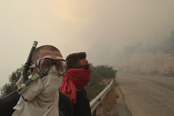 Люди закрывают лица от дыма во время лесного пожара возле Кинеты, к западу от Афин. 23 июля 2018 года