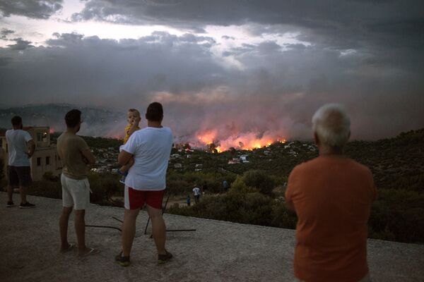 Люди наблюдают за лесным пожаром в городе Рафина, недалеко от Афин. 23 июля 2018 года