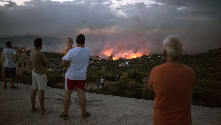 Люди наблюдают за лесным пожаром в городе Рафина, недалеко от Афин. 23 июля 2018 года