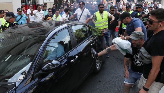 Участник забастовки таксистов в Барселоне пинает автомобиль, работающий с сервисом Uber. 25 июля 2018