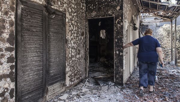 Женщина у своего дома, пострадавшего в результате лесных пожаров, в поселении Мати в Греции. 25 июля 2018