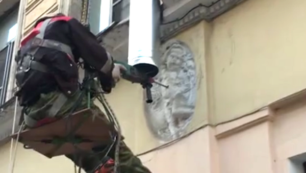 Стоп-кадр с видео, где рабочий сверлит барельеф с изображением ангела на фасаде дома №1 на Ропшинской улице в Санкт-Петербурге. 8 августа 2018