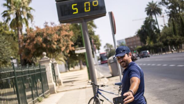 Мужчина фотографируется у электронного табло, которое показывает температуру +50 градусов по Цельсию на улицах города Севилья в Испании
