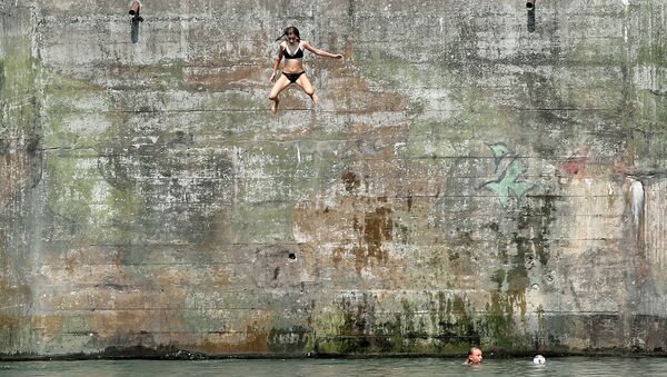 Девушка прыгает в воду в жаркий летний день из старого бункера в районе Нойхаузен-ам-Райнфалль, Швейцария. 6 августа 2018 года