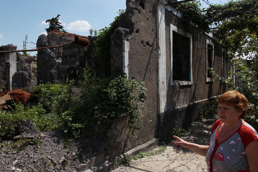 Женщина показывает соседние дома, разрушенные при обстрелах. Донецкая народная республика