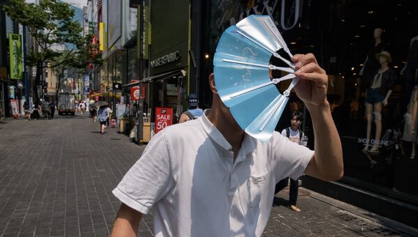 Прохожий закрывает лицо веером во время жары в Сеуле. 1 августа 2018