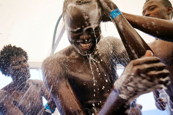 Семнадцатилетний беженец из Судана принимает душ после спасения лодки с мигрантами в Средиземном море